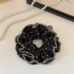 Detailed texture of black floral scrunchie with white lace edges and soft fabric