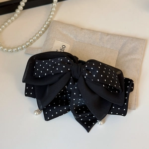 Détail d'une pince à cheveux à nœud noir à pois avec d'élégantes perles suspendues