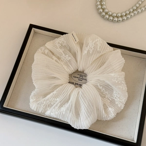 Detail of white pleated mesh scrunchie with lace embroidery and a handmade label