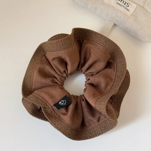 Close-up of brown ruffled fabric scrunchie texture with a small black brand label
