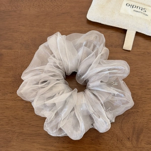 Détail macro du chouchou en organza champagne avec paillettes argentées sur bois