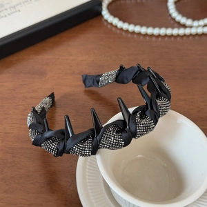 Close-up of luxury punk headband with black spikes and crystals on white ceramic cup