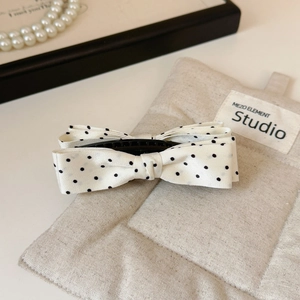 Dettaglio del fermaglio per capelli a fiocco bianco con pois neri e consistenza satinata