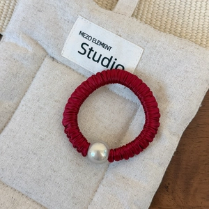Détail d'un chouchou en satin rouge avec grande perle argentée sur fond en lin beige