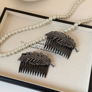 Detailed view of leaf-shaped hair combs with dark gray rhinestones on a beige tray