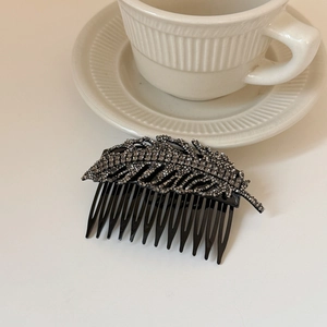 Detailed view of leaf-shaped hair comb with dark rhinestones on a white ceramic tray