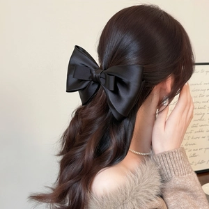 Dettaglio di un elegante fiocco nero in raso a doppio strato indossato sui capelli mossi