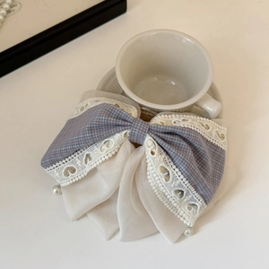 Detail of lavender plaid bow hair clip with lace edges and pearls on a ceramic cup
