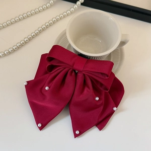 Close-up of wine red satin bow hair clip with pearls and elegant pearl necklace decor