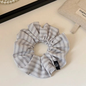 Detail of grey striped fabric scrunchie with branded label on a minimalist background