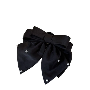 Elegant black bow hair clip with white pearl accents on minimalist white background