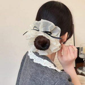 Vue détaillée du chouchou en organza crème avec un nœud en ruban noir et des volants