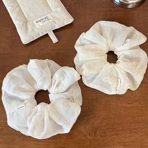 Detail of white scrunchies with butterfly embroidery and handmade tag on wood surface