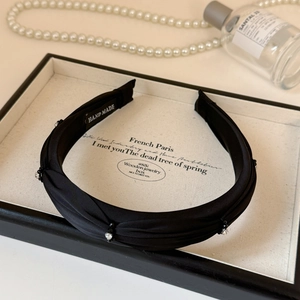Detail of black pleated fabric headband with small rhinestones and hand made label