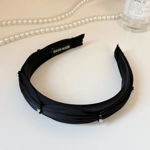 Detail view of black pleated satin headband with rhinestones and handmade label