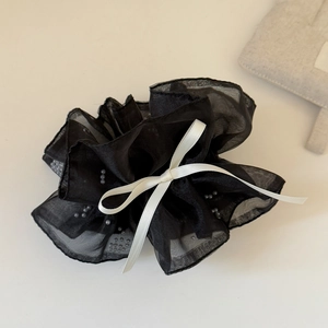 Détail d'un chouchou en maille noire avec perles argentées et un nœud en ruban blanc