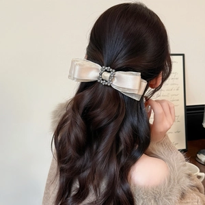 Elegant champagne silk bow hair clip with rhinestone buckle on long wavy brown hair