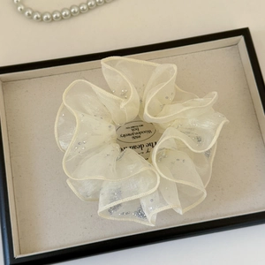 Détail macro d'un chouchou en tulle crème orné de paillettes argentées scintillantes