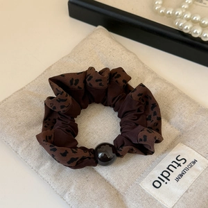 Detailed view of coffee leopard print scrunchie with a brown bead on beige linen fabric