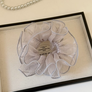Vue macro d'un chouchou en organza gris avec paillettes argentées et bords ondulés drapés