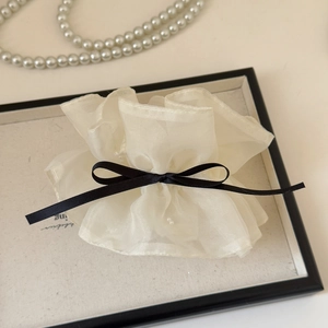 Gros plan d'un chouchou en organza blanc avec nœud noir et détails de perles fines