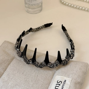 Détail d'un serre-tête de luxe avec strass argentés et pointes punk noires sur coussin