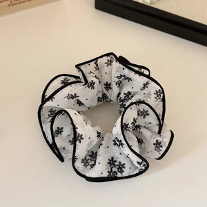Gros plan d'un chouchou à fleurs avec bord noir sur une surface de couleur crème
