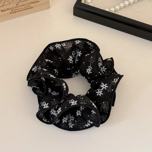 Gros plan d'un chouchou noir à fleurs blanches sur un fond blanc épuré
