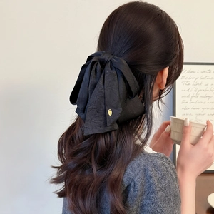 Elegant large black fabric bow hair clip with gold metal tag on model's dark brown hair