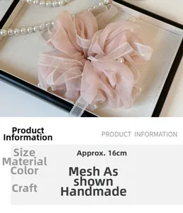 Détail d'un chouchou en organza rose de 16cm avec bord en dentelle sur un plateau blanc