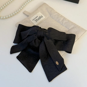 Detail of elegant black satin bow hair clip with shimmering rhinestones and gold tag