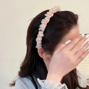 Dettaglio di fascia in tulle rosa chiaro con texture a pieghe e ciondolo cuore d'oro