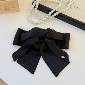 Close-up of a large black satin bow clip with delicate textures and a gold logo tag