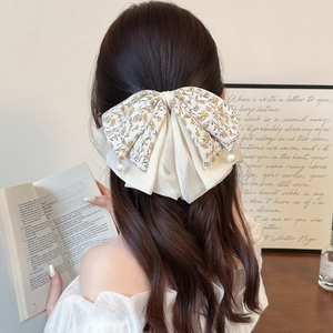 Elegant double-layered bow hair clip with floral print and pearls worn by a model