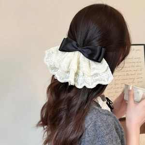 Close-up of elegant black satin bow with layered lace embroidery on hair clip