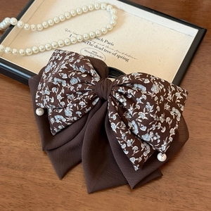 Detail of vintage bow hair clip with dark floral fabric and elegant white faux pearls