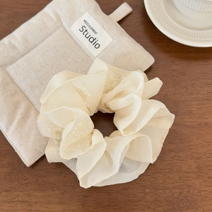 Close-up of cream organza scrunchie with embedded white pearls on a wooden surface