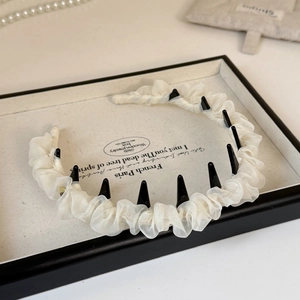 Dettaglio del cerchietto in chiffon bianco sporco con texture pieghettata e denti a pettine neri
