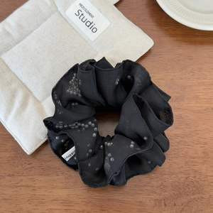 Detail of black mesh hair scrunchie with pearls and woven label on wood surface