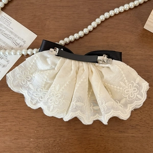 Elegant white lace bow hair clip with black satin base on a vintage wooden desk