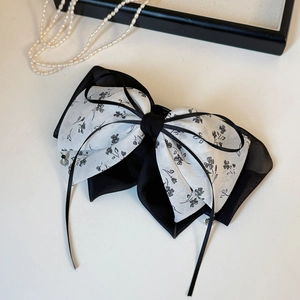 Détail d'une pince à cheveux à double nœud floral avec d'élégants rubans noirs fluides