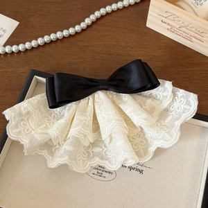 Detailed close-up of a satin black bow hair clip with tiered cream lace on a display tray