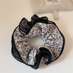 Dettaglio macro dello scrunchie floreale oversize con bordo in pizzo a rete nera a strati