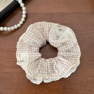 Detail of checkered scrunchie with white lace edges on a dark wood background