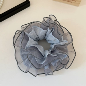 Detail of light blue organza scrunchie with grey trim and layered pleats on white surface