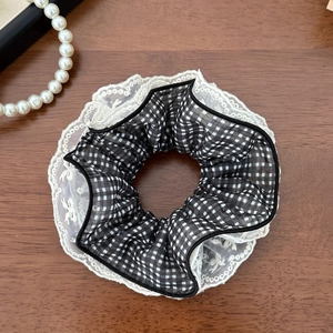 Close-up of black and white plaid scrunchie with layered white lace details on wooden surface