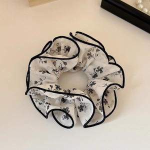 Détail d'un chouchou floral blanc cassé avec motifs de fleurs noires et bordure