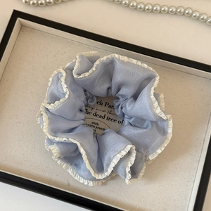 Detail of light blue organza scrunchie with white ruffle edges on a display tray