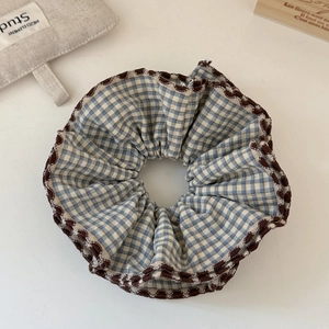 Detail of blue and white plaid hair scrunchie with brown wavy ruffled edges and cotton texture