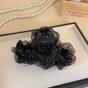 Détail d'une pince à cheveux rose en résille noire avec paillettes argentées sur plateau